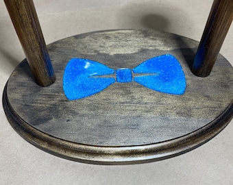 May include: A wooden stand with two upright posts and a round base. The base has a blue bowtie design with glitter.