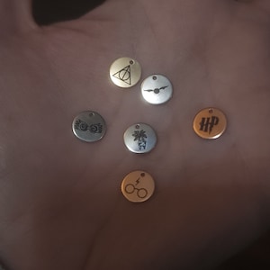 May include: Six silver and gold charms with Harry Potter symbols. The charms include the Deathly Hallows symbol, a snitch, a pair of glasses with a lightning bolt, a pair of glasses with wings, a tree, and the letters HP.
