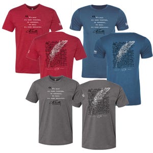 Puede incluir: Una colección de camisetas de manga corta en rojo, azul y gris. Cada camiseta presenta una cita y una firma en la parte delantera, con un diseño de pluma y escritura en la parte trasera. El texto incluye el año 1776.