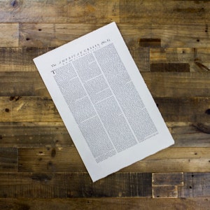 以下が含まれることがあります： 白い背景に黒いインクで「The American Crisis (No. 1)」というタイトルが印刷された、ビンテージの新聞印刷。新聞は木製の表面に平らに置かれている。