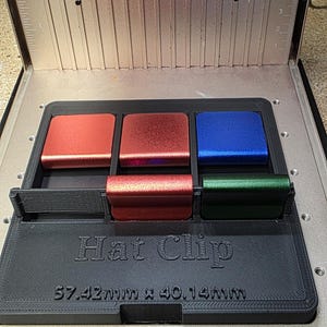 May include: A black Hat Clip with four colored hat clips: red, red-orange, blue, and green. The Hat Clip is 57.42mm x 40.14mm. The device is inside a metal enclosure with a fan.