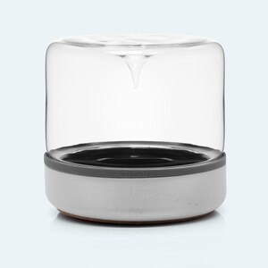 May include: A white ceramic planter with a gray silicone ring and a clear glass dome. The planter has the word "bioasis" printed on the side.