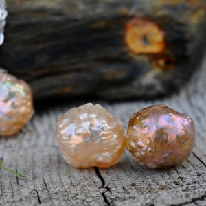 May include: Three iridescent pink pearls with a textured surface. The pearls are on a wooden surface.