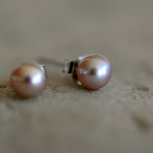 May include: A pair of pearl stud earrings with silver posts. The pearls are a soft pink color.