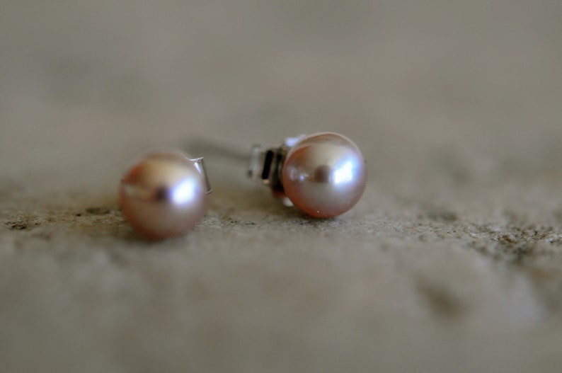 May include: A pair of pearl stud earrings with silver posts. The pearls are a soft pink color.