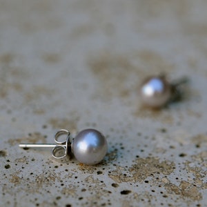 May include: A pair of silver stud earrings with a single pearl on each. The pearls are a light gray color.