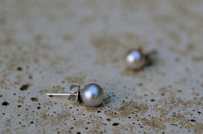 May include: A pair of silver stud earrings with a single pearl on each. The pearls are a light gray color.
