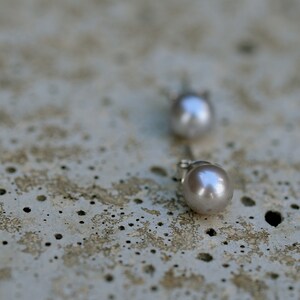 May include: A pair of silver stud earrings with a pearl on each. The pearls are a light gray color.