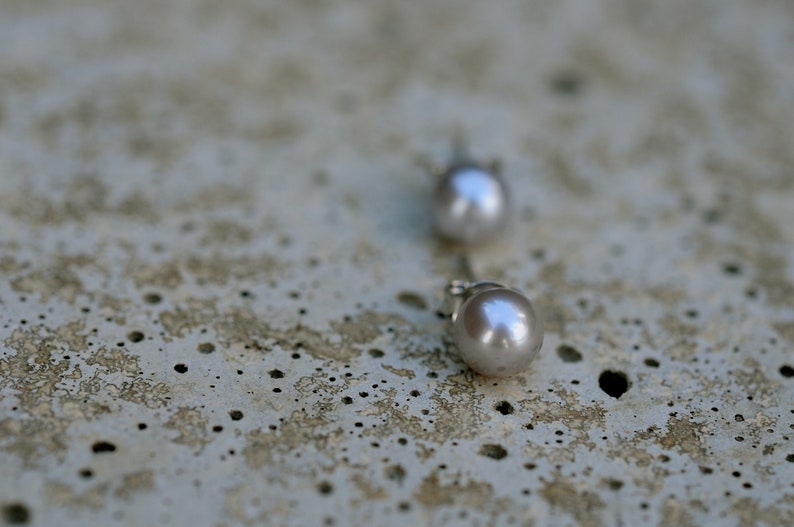 May include: A pair of silver stud earrings with a pearl on each. The pearls are a light gray color.