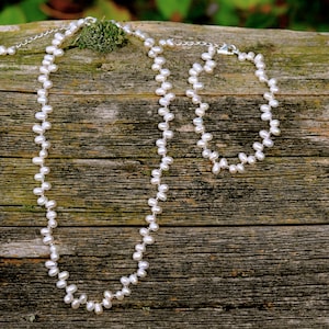 May include: A white pearl necklace and bracelet set on a rustic wooden background. The necklace and bracelet are made of small, round pearls.