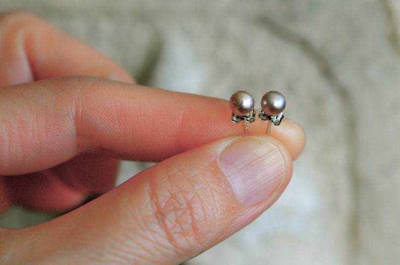 May include: A pair of silver stud earrings with small, round, light purple pearls.