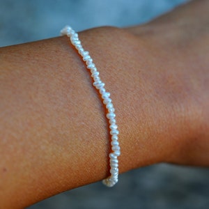 Puede incluir: Un delicado brazalete de perlas blancas con pequeñas perlas espaciadas uniformemente.