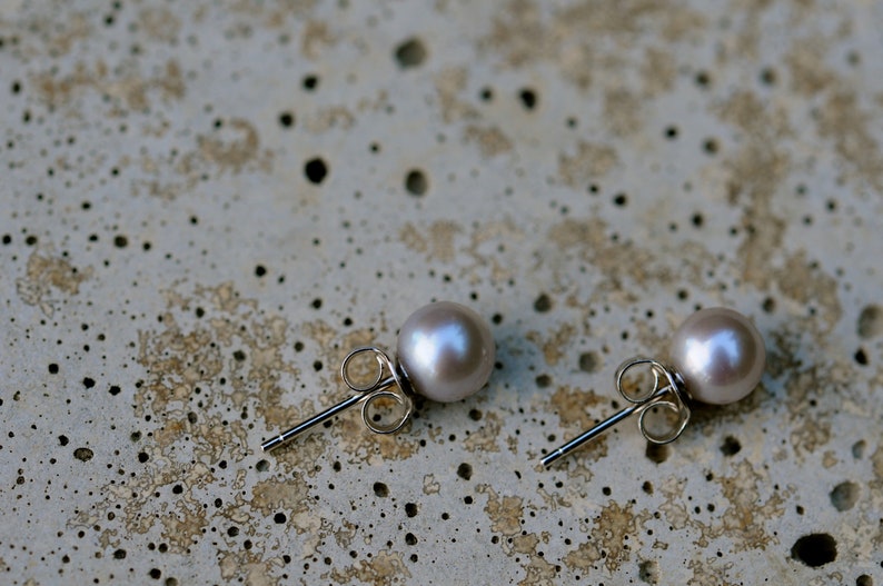 May include: A pair of silver stud earrings with a light purple pearl on each earring.