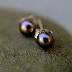 May include: A pair of silver stud earrings with black pearl accents. The pearls are round and have a slight iridescent sheen.