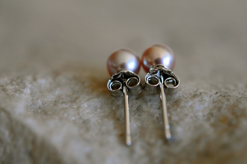 May include: A pair of silver stud earrings with pink pearl accents.