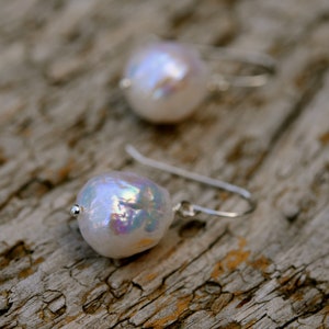 May include: A pair of silver earrings with iridescent white pearl drops. The pearls have a subtle shimmer and are suspended from delicate silver hooks.