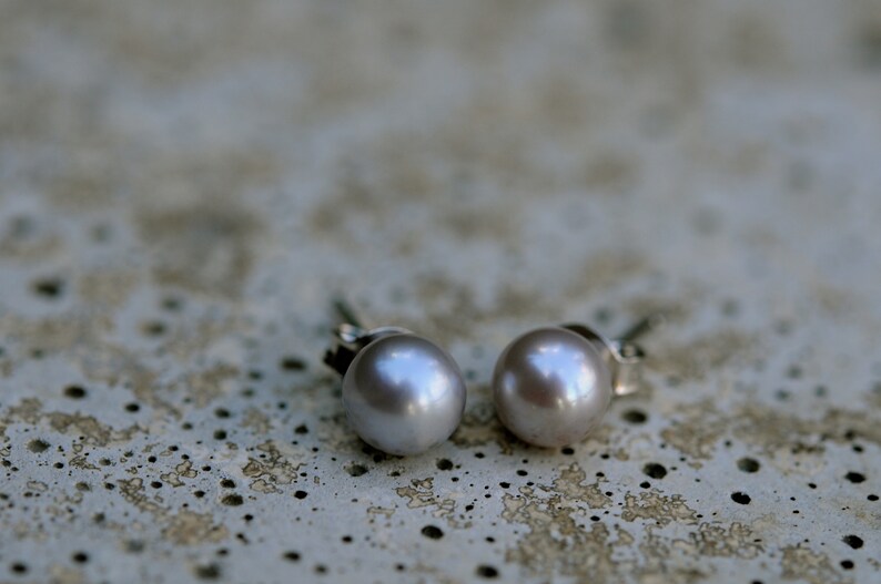 May include: A pair of silver stud earrings with a light gray pearl on each earring.