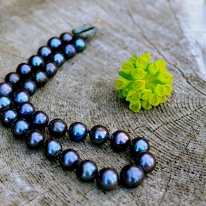 May include: A strand of black pearls on a wooden surface with a small yellow flower.