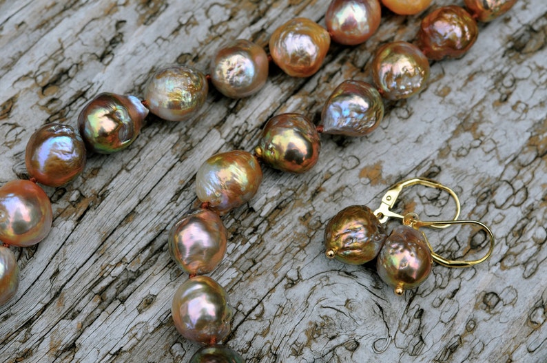 K&ouml;nnte beinhalten: Eine Kette aus irisierenden Perlen in Braun-, Rosa- und Goldt&ouml;nen mit passenden Ohrringen. Die Perlen sind auf einem d&uuml;nnen Draht aufgef&auml;delt und haben eine nat&uuml;rliche, unregelm&auml;&szlig;ige Form.