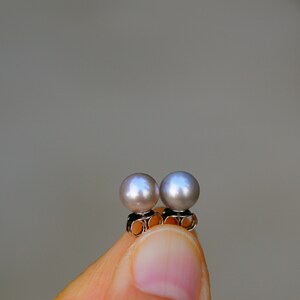May include: A pair of pearl earrings with silver posts. The pearls are a light gray color.