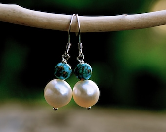 Op de afbeelding: Een paar zilveren oorhangers met turquoise en witte parels.