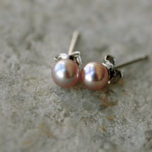 May include: A pair of pearl stud earrings with silver posts. The pearls are a light pink color.