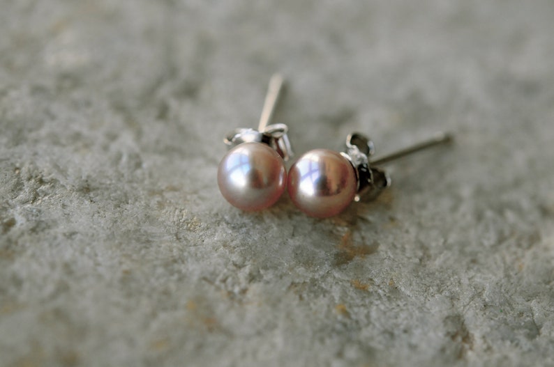 May include: A pair of pearl stud earrings with silver posts. The pearls are a light pink color.