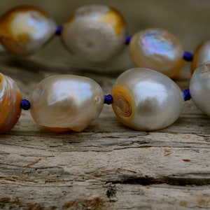 May include: A strand of large, white and brown pearls with a blue cord threaded through the pearls.