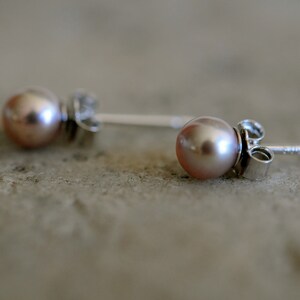 May include: A pair of silver stud earrings with a light pink pearl on each earring.