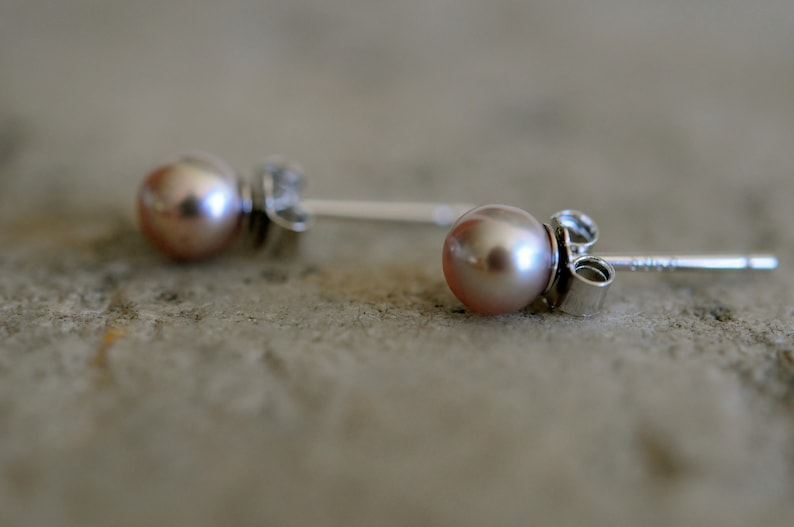 May include: A pair of silver stud earrings with a light pink pearl on each earring.