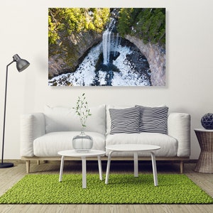 May include: An aerial view of a waterfall cascading down a rocky cliff, surrounded by lush green trees. The water is clear and white, and the surrounding area is covered in snow.