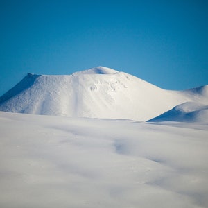 May include: A snow-covered mountain range with a bright blue sky in the background.