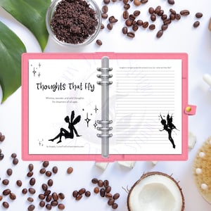 May include: A pink binder notebook with the text "Thoughts That Fly" and illustrations of fairies and stars. The notebook is open to lined pages, with coffee beans and a bowl of ground coffee surrounding it.