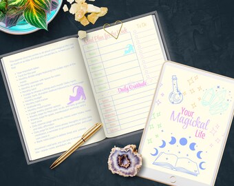 May include: An open planner with a gold pen, a tablet, and a decorative stone. The planner has sections for meal planning and daily gratitude. The tablet displays the text "Your Magickal Life" with illustrations of crystals and moons.