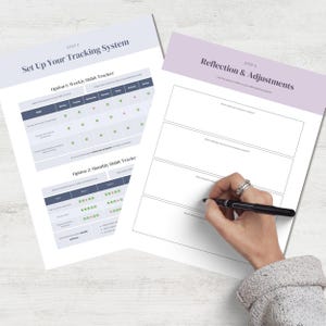 May include: Two white sheets of paper with text and tables for tracking habits. One sheet says "Set Up Your Tracking System" and the other says "Reflection & Adjustments." A hand with a pen is writing on the second sheet.