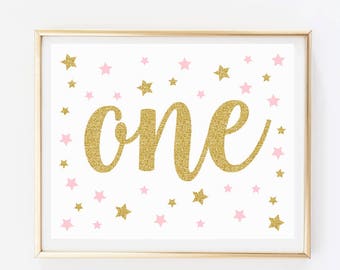 May include: Gold glitter "one" with pink glitter stars on a white background in a gold frame.