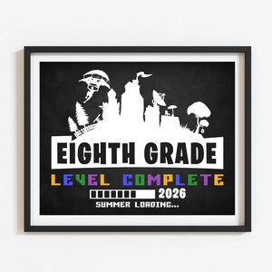 May include: A framed print with a black border features a white silhouette of a cityscape and the words "EIGHTH GRADE LEVEL COMPLETE 2026 SUMMER LOADING..." in a colorful font against a black background.