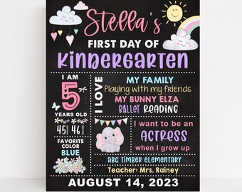 May include: A chalkboard sign with a pink and purple design announcing a girl's first day of kindergarten. The sign includes her name, age, favourite colour, and interests. It also includes the name of her school and teacher. The date is 14 August 2023.