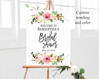 May include: A white sign on a wooden easel with floral accents. The sign reads "WELCOME TO SAMANTHA'S Bridal shower MAY 12, 2018". The sign has a watercolor floral design with pink and yellow flowers.