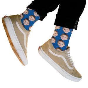 May include: A pair of blue socks with a repeated pattern of a person's face. The socks are being worn by a person wearing beige sneakers.