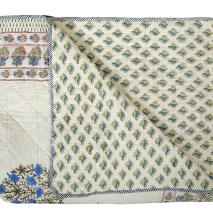 Puede incluir: Una colcha de algod&oacute;n blanco con un patr&oacute;n floral azul y verde. La colcha est&aacute; doblada por la mitad y tiene un fondo blanco con un patr&oacute;n floral azul y verde.
