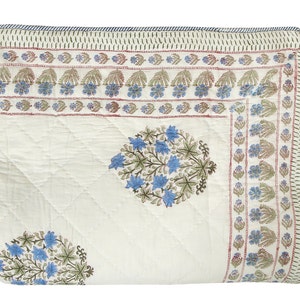 Puede incluir: Una colcha de algod&oacute;n blanco con estampado floral azul y verde. La colcha tiene un borde con un patr&oacute;n floral repetitivo.