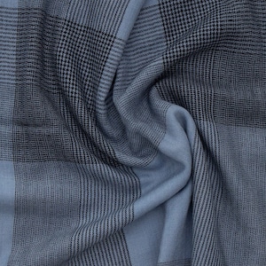 May include: A close-up of a blue and black plaid fabric. The fabric is folded and wrinkled, showing the texture of the material.