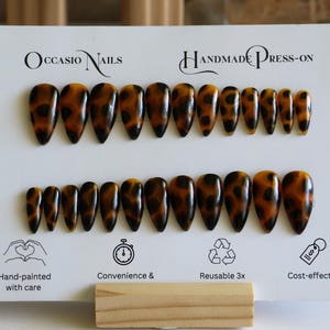 May include: A set of handmade press-on nails with a tortoiseshell design. The nails are almond-shaped and feature a pattern of dark brown spots on a light brown background. The card reads "Occasio Nails" and "Handmade Press-on".