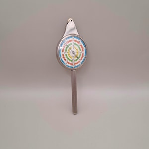 May include: A vintage silver map measurer with a colourful circular dial. The dial has concentric rings of red, blue, green, and yellow. The handle is ribbed, and the top has a small hole. This tool is used for measuring distances on maps.