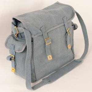 May include: A light blue canvas shoulder bag with adjustable straps and brass buckles. The bag has a flap closure and a large main compartment.