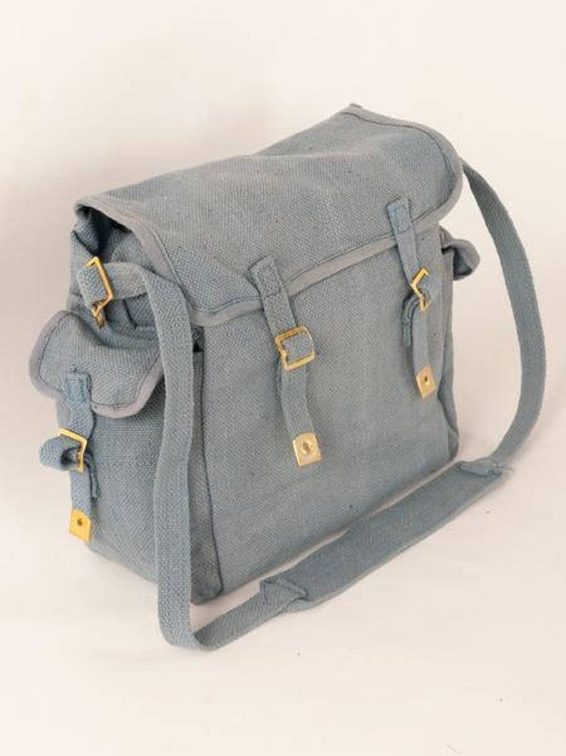 May include: A light blue canvas shoulder bag with adjustable straps and brass buckles. The bag has a flap closure and a large main compartment.