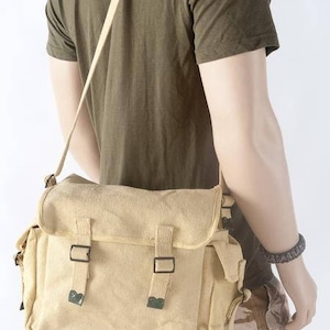 May include: A beige canvas messenger bag with two adjustable straps and a flap closure. The bag has a large main compartment and two smaller pockets on the front.