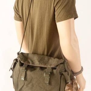 May include: A green canvas messenger bag with a flap closure and adjustable strap. The bag has two buckles on the front and a zippered pocket on the side.