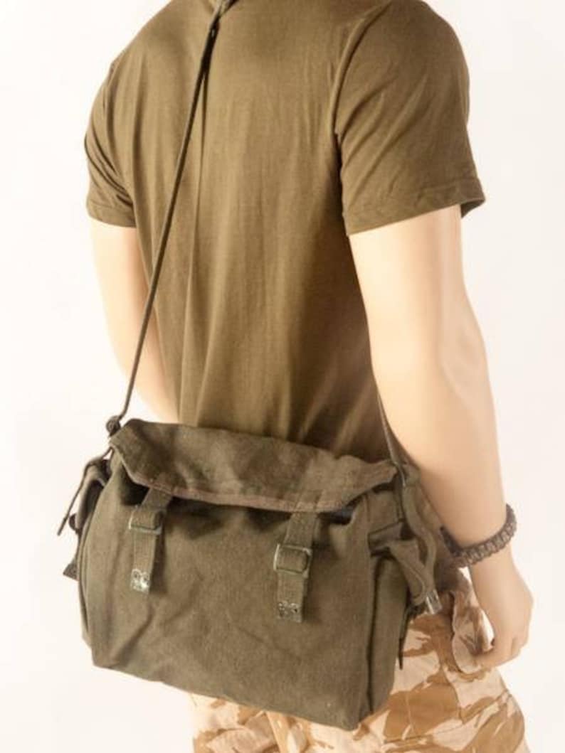 May include: A green canvas messenger bag with a flap closure and adjustable strap. The bag has two buckles on the front and a zippered pocket on the side.